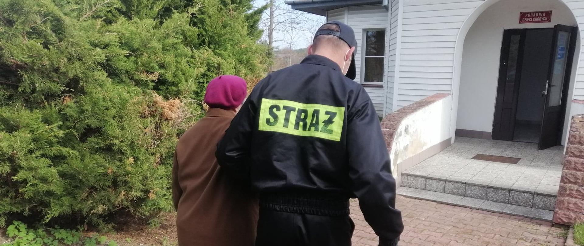 Strażak OSP odprowadza osobę do punktu szczepień.