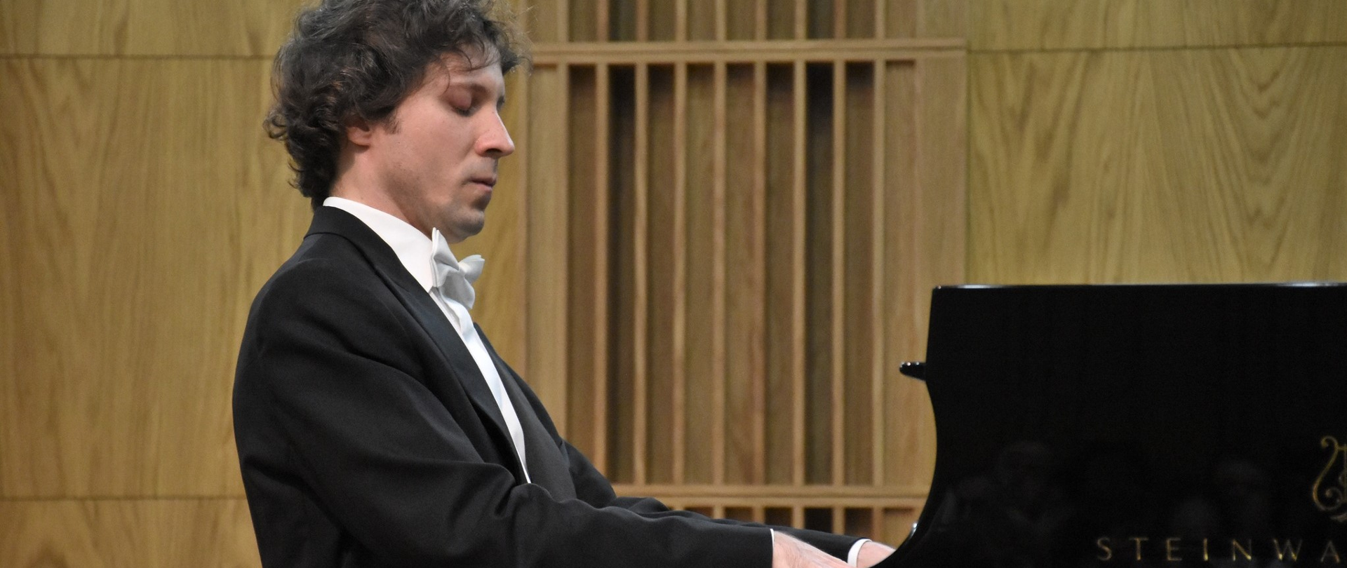 Zdjęcia przedstawia Pianistę Rafała Blechacza w trakcie wykonywania koncertu w PSM I stopnia w Zambrowie. Pianista jest skupiony i patrzy na swoje ręce. W prawym dolnym rogu widać fragment logo fortepianu stainway&sons