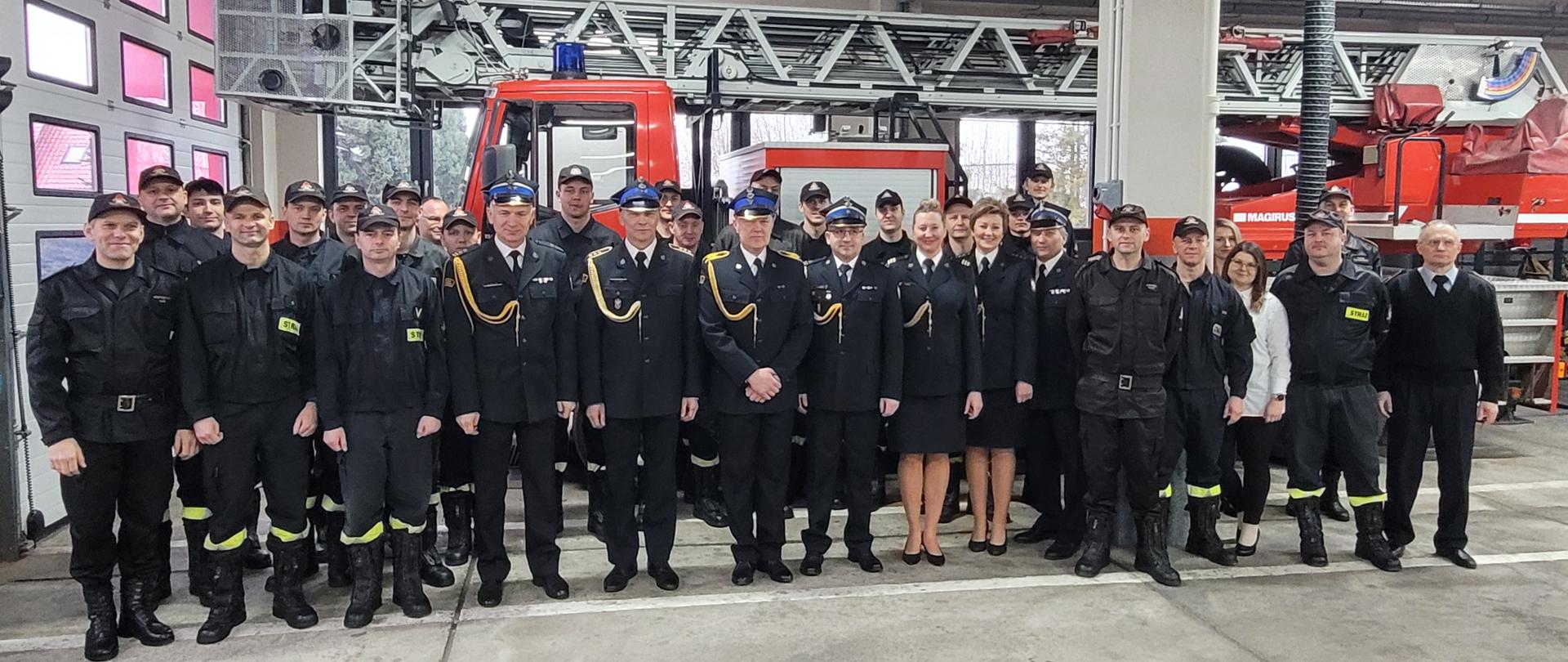 Na zdjęciu grupowym strażacy w mundurach wyjściowych i służbowych stoją na tle drabiny pożarniczej