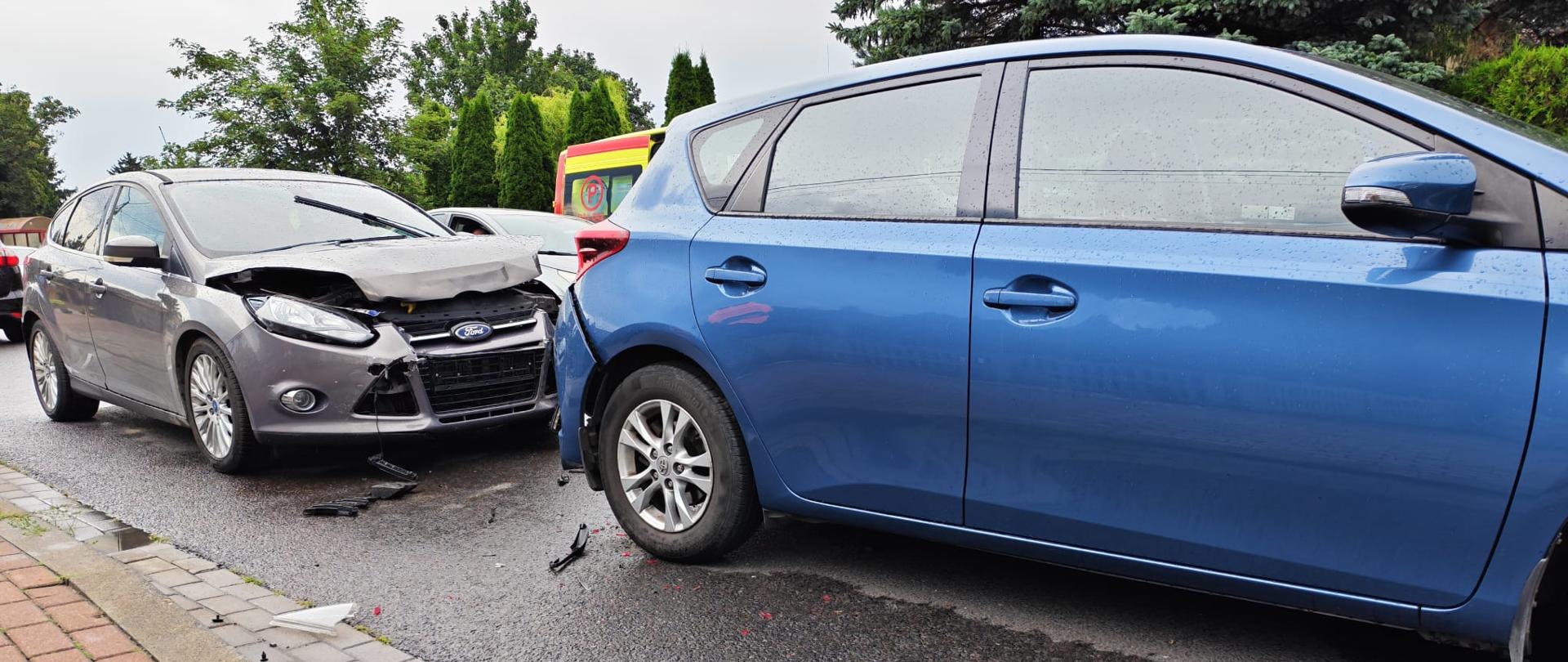 ChatGPT powiedział:
Na zdjęciu widoczna jest scena po kolizji dwóch samochodów osobowych na ulicy. Szary samochód marki Ford uderzył w tył niebieskiego pojazdu, powodując znaczne uszkodzenia przodu swojego auta – zgnieciona maska, uszkodzony zderzak i widoczne fragmenty plastiku na jezdni. Niebieski samochód ma lekko wgnieciony tył. W tle widoczny jest ambulans i fragmenty innych pojazdów. Droga jest mokra, co może sugerować niedawną opad atmosferyczny.