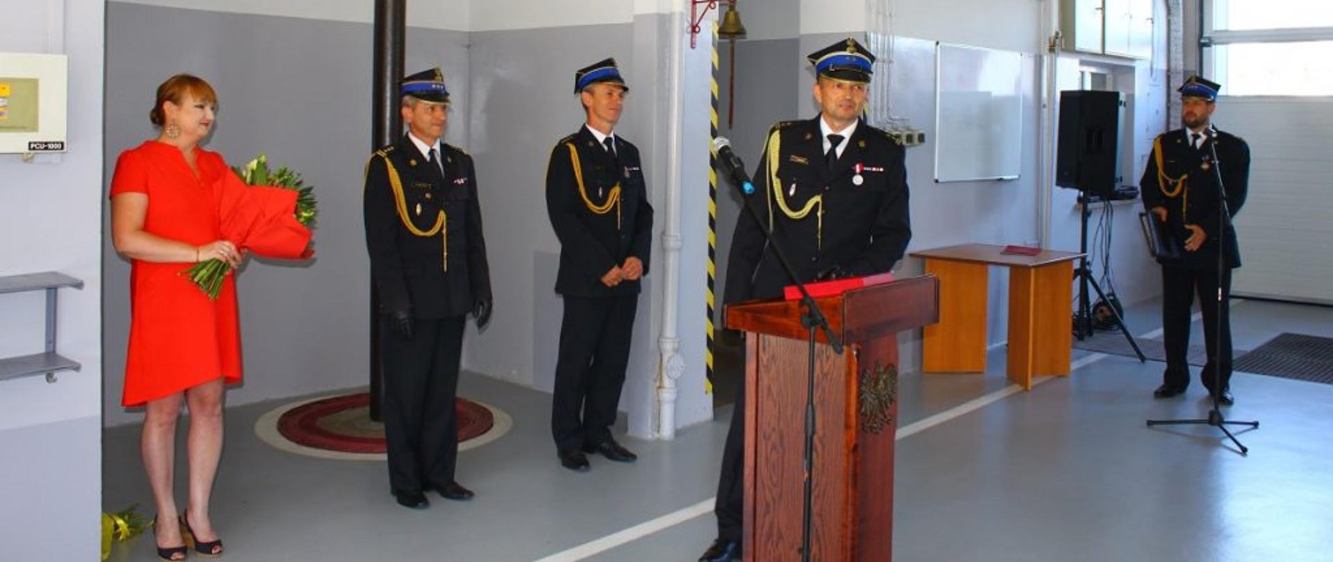 Brygadier Zbigniew Dudzik w mundurze wyjściowym podczas przemówienia okolicznościowego obok najbliższa rodzina i kierownictwo komendy