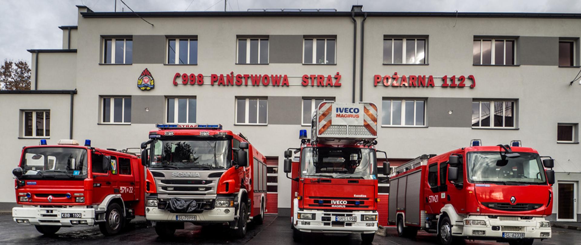 Zdjęcie frontu budynku Komendy Miejskie Państwowej Straży Pożarnej w Rudzie Śląskiej wraz z stojącymi przed nią samochodami pożarniczymi.