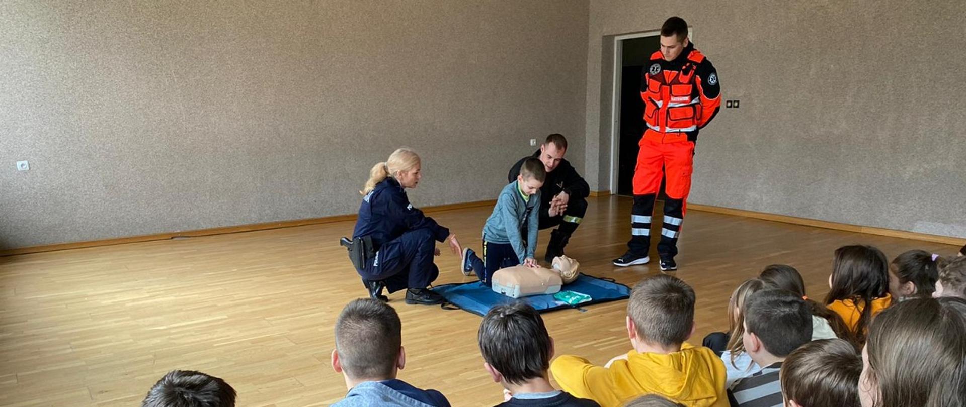 Na zdjęciu widać Strażaka, Policjantkę i Ratownika KGPP zaznajamiający młodzież z zasadami udzielania pierwszej pomocy osobom poszkodowanym