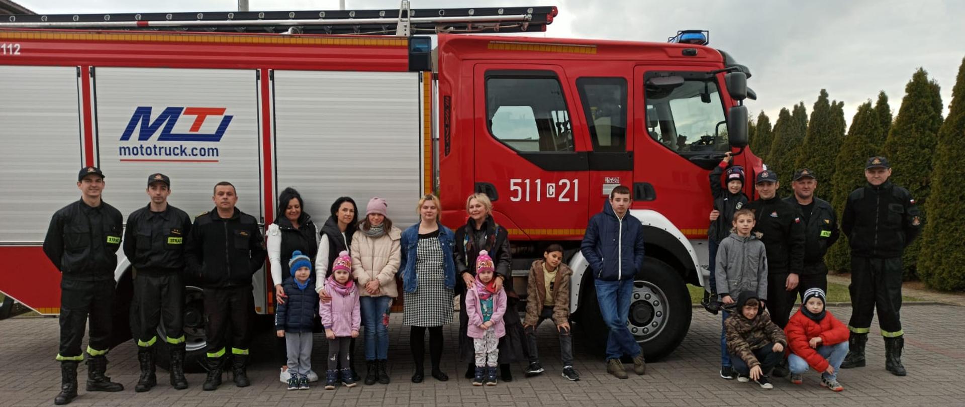 Na tle specjalnego samochodu gaśniczego do zdjęcia ustawionych jest sześciu strażaków z Komendy Powiatowej Państwowej Straży Pożarnej w Rypinie. Razem z nimi stoi jedenaście dzieci z Domu Dziecka im. Janusza Korczaka w Rypinie, wraz z trzema opiekunkami. Wszyscy znajdują się na placu komendy.