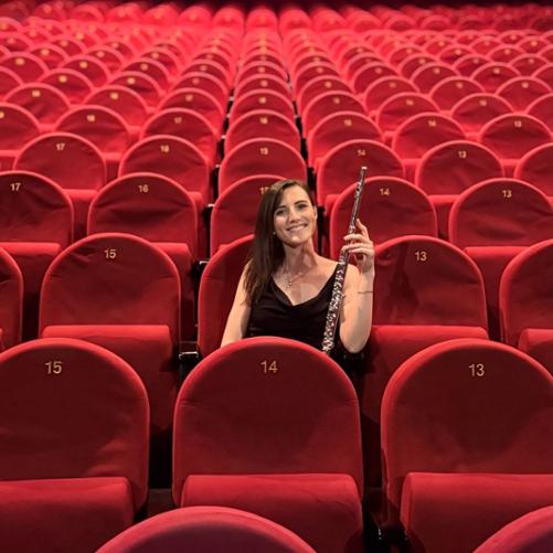 Kobieta siedzi na pustek widowi i trzyma flet.