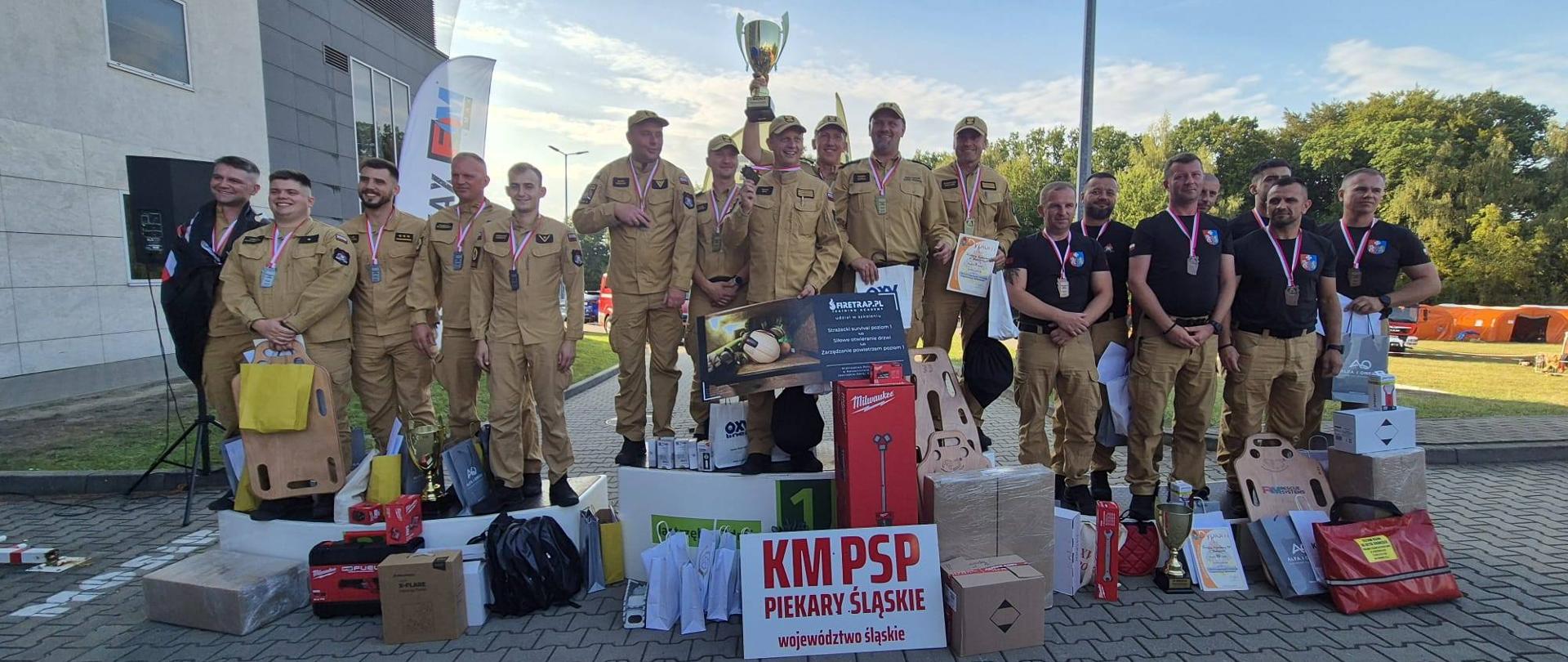 Zdjęcie przedstawia Strażaków Państwowej Straży Pożarnej stojących na podium podczas Mistrzostw Polski Strażaków w Ratownictwie Technicznym o Puchar Komendanta Głównego Państwowej Straży Pożarnej.