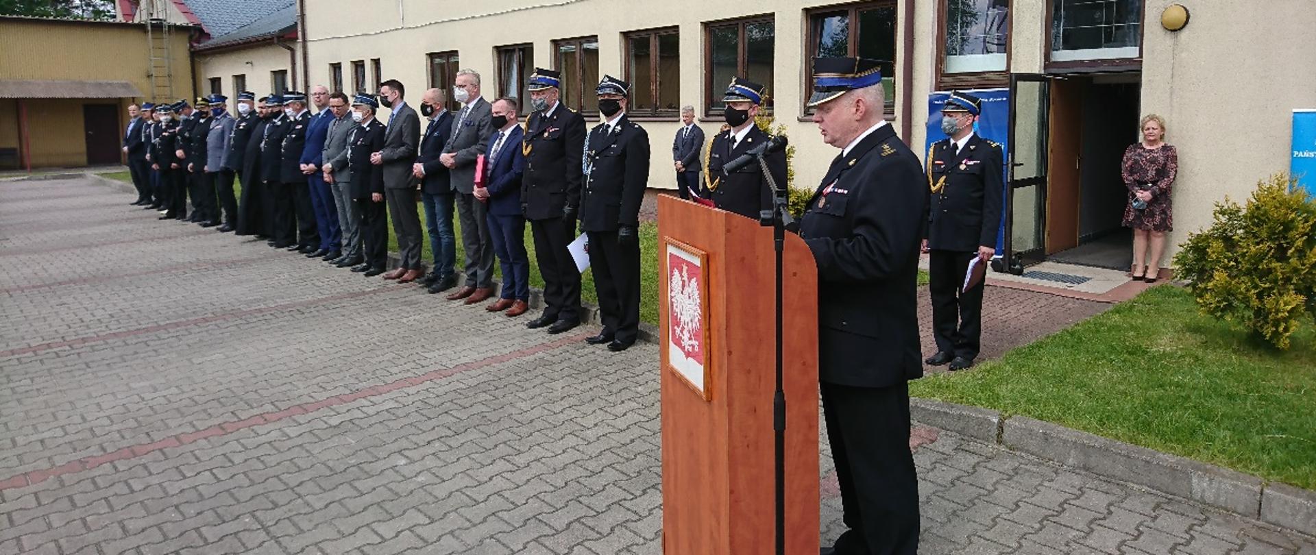 Na pierwszym planie przy mównicy wita gości Komendant Powiatowy PSP w Wołominie, w tle zaproszeni goście