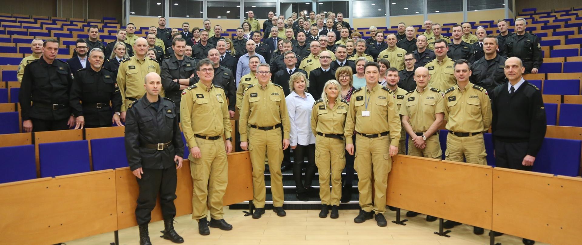 Na auli grupa funkcjonariuszy pozuje na stojąco do zdjęcia