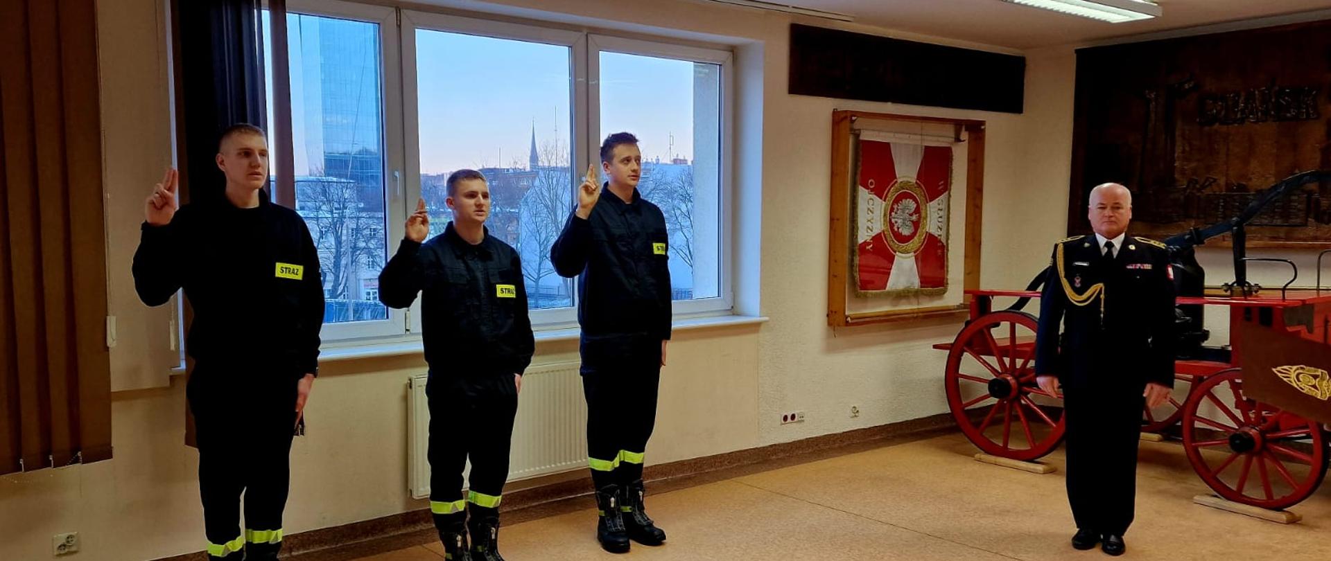 3 funkcjonariuszy składa ślubowanie na świetlicy JRG 1. Obok zastępca dowódcy JRG 1.