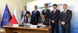 Przedstawiciel PLK SA i wykonawcy podpisują umowę na linię 104. W tle minister infrastruktury Dariusz Klimczak oraz wiceminister infrastruktury Piotr Malepszak