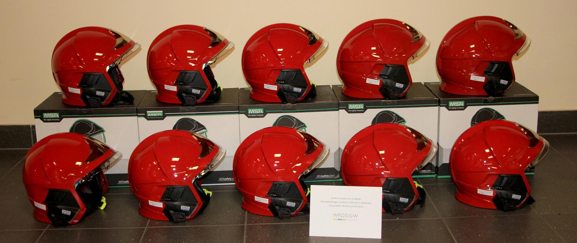 Czerwone hełmy strażackie widoczne z boku stoi na kartonach i na podłodze.