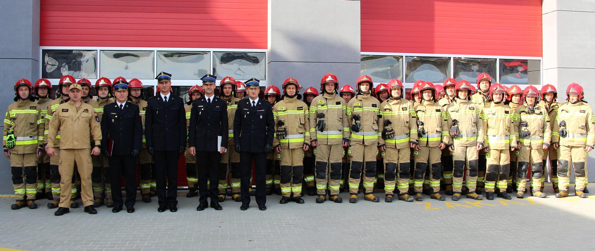 Na zdjęciu przedstawiono strażaków z ze zmian 2 i 3 z Jednostki Ratowniczo-Gaśniczej nr 1 na tle budynku strażnicy. Wśród nich na pierwszym planie od lewej: dowódca JRG nr 1, naczelnik Wydziału Operacyjnego-Kadrowego, zastępca komendanta miejskiego, nowy zastępca dowódcy JRG nr 1 i komendant miejski PSP w Kielcach
