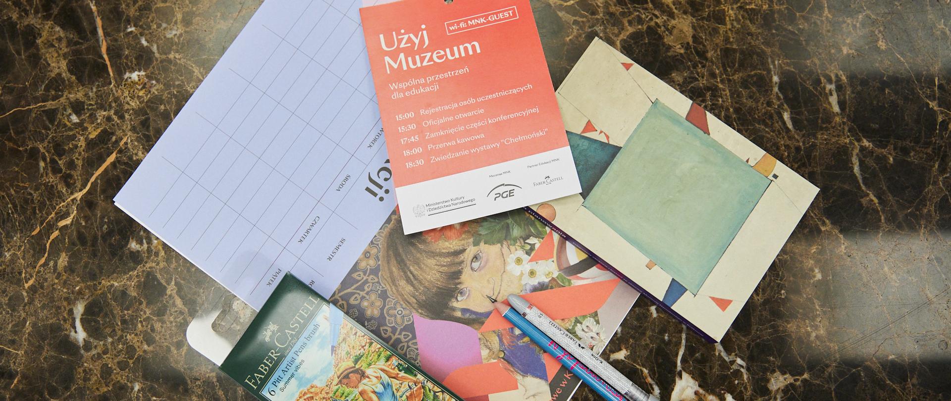 Na marmurowym blacie materiały edukacyjne oraz przybory przygotowane na warsztaty w muzeum, związane z zajęciami artystycznymi.