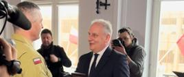 Wojewoda pomorski wręcza medal strażakowi obok stoją dziennikarze z kamerą, aparatem fotograficznym.
