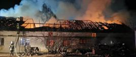 strażacy prowadzą działania gaśnicze na obiekcie objętym pożarem - widać ruiny więźby dachowej, łunę ognia i wydobywający się dym