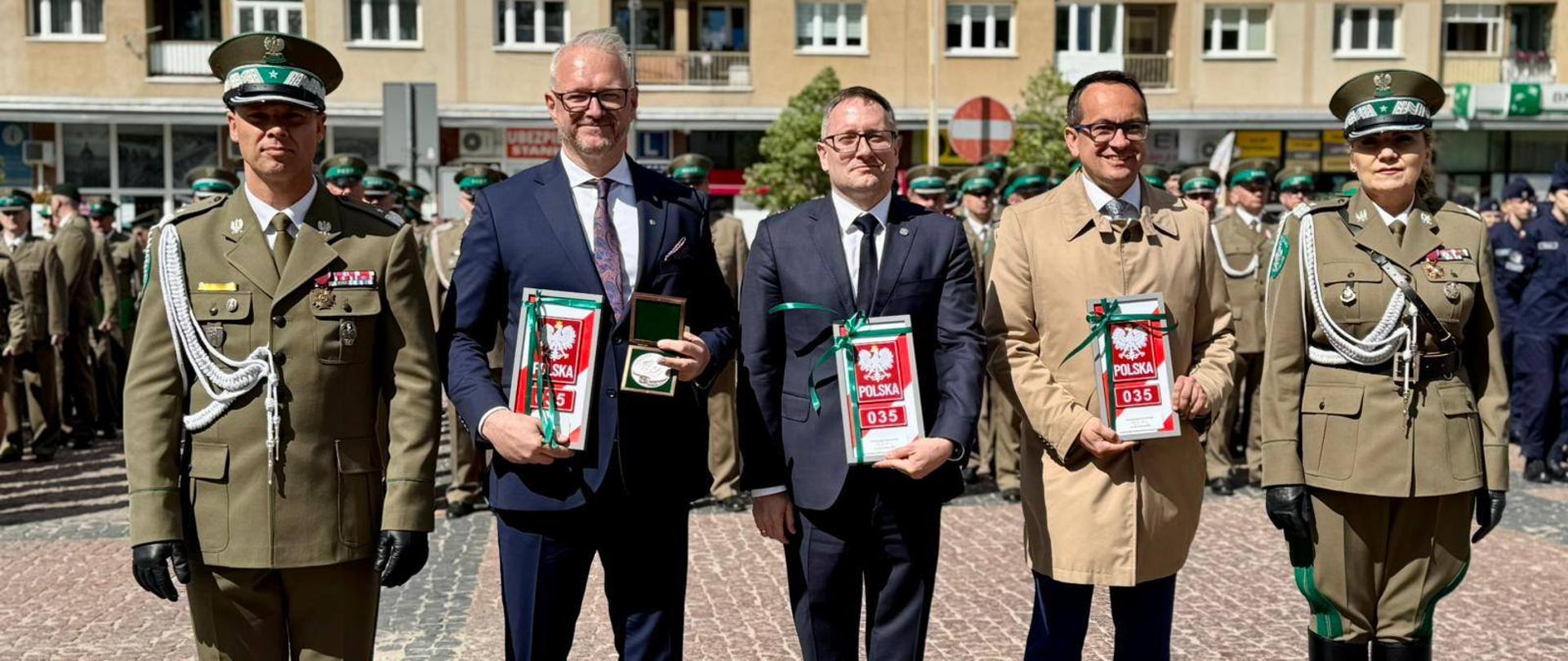 mężczyzna w garniturze, wojewoda, pozuje do zdjęcia, trzyma w ręku prezent z godłem Polski 