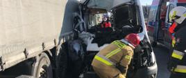 uszkodzony samochód (bus) w wyniku wypadku stojący obok naczepy samochodu ciężarowego, obok pojazdów stoją strażacy