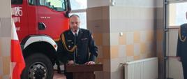 Zdjęcie przedstawia odchodzącego na emeryturę komendanta podczas przemówienia, w tle widać samochód pożarniczy.