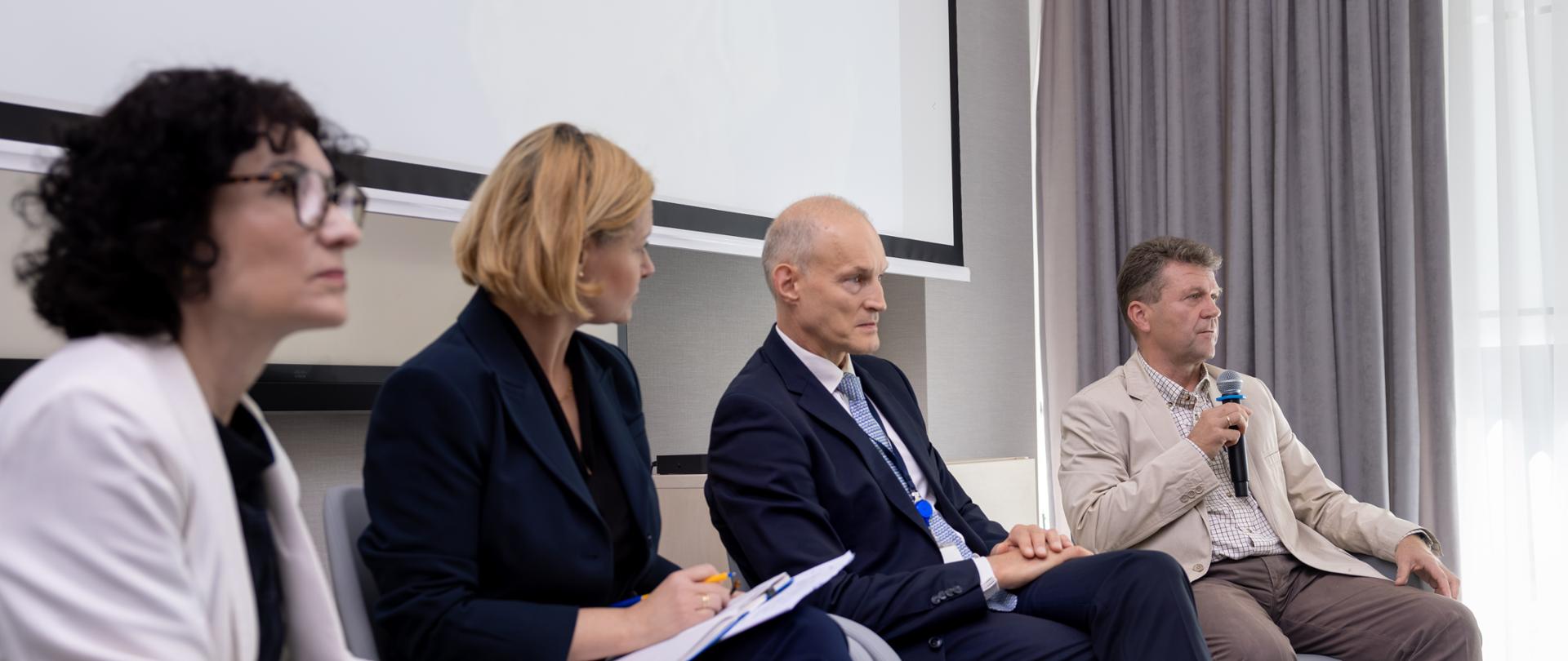2 kobiety i 2 mężczyzn siedzi na krzesła w ramach panelu dyskusyjnego, wśród nich wiceminister Zajączkowski