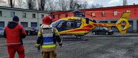 Zdjęcie przedstawia kierującego działaniem ratowniczym oraz jednego z ratowników medycznych zmierzających w kierunku śmigłowca.