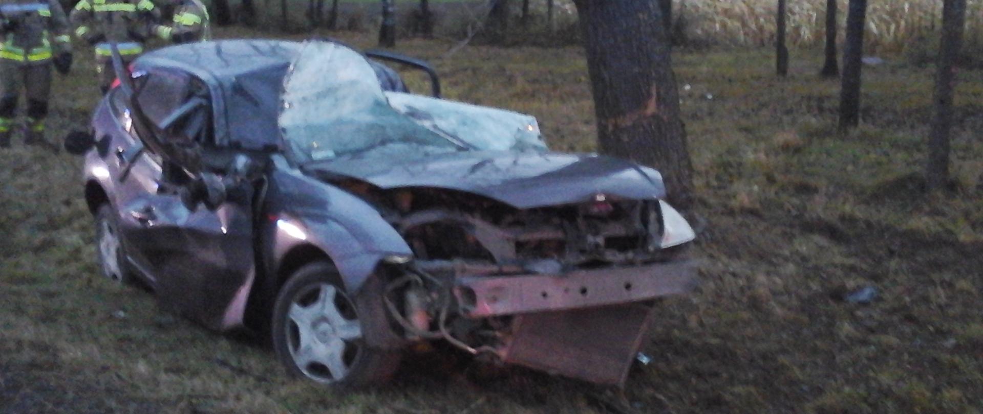Rozbity samochód osobowy stojący w przydrożnym rowie. Samochód całkowicie zniszczony po uderzeniu w przydrożne drzewo. 