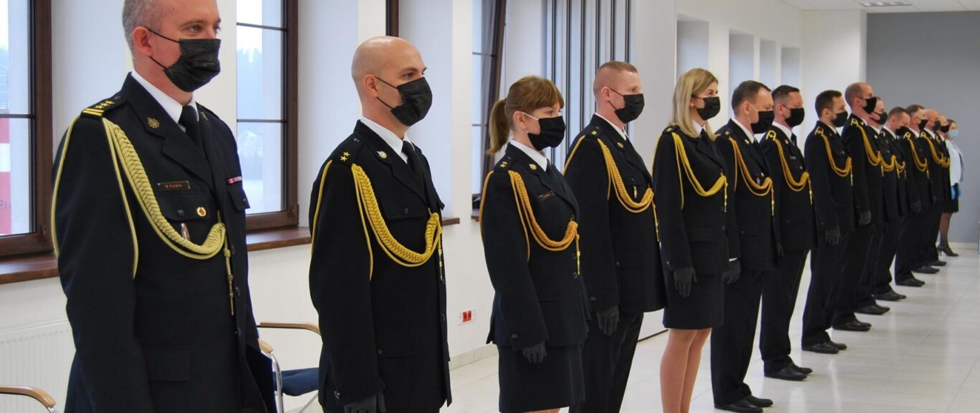 Na zdjęciu szereg strazaków w umundurowaniu galowym podczas uroczystej zbiórki z okazji nadania wyższych stopni służbowych.