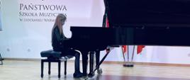 Dziewczynka gra na fortepianie, w tle napis Państwowa Szkoła muzyczna w Lidzbarku Warmińskim.