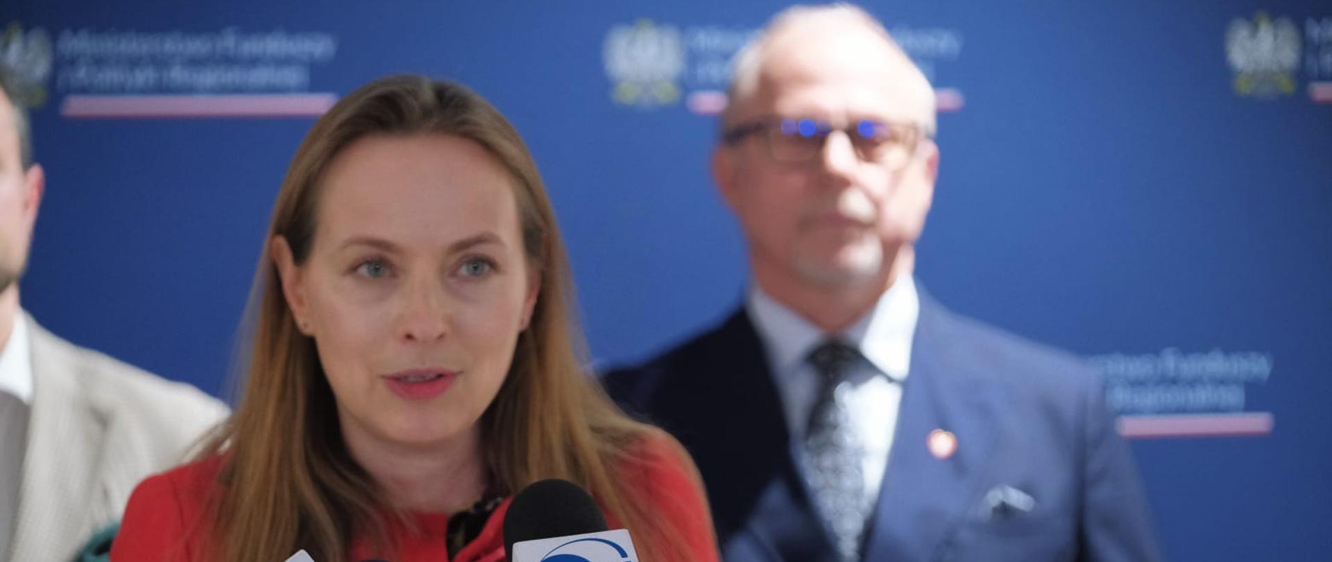 Minister Katarzyna Pełczyńska-Nałęcz stoi przy dwóch mikrofonach.