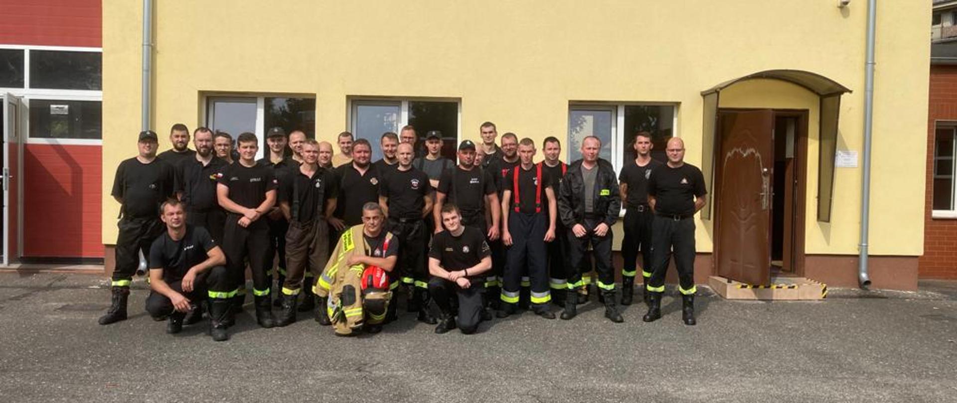 Zdjęcie grupowe strażaków OSP biorących udział w szkoleniu-kursie. W tle remiza PSP.