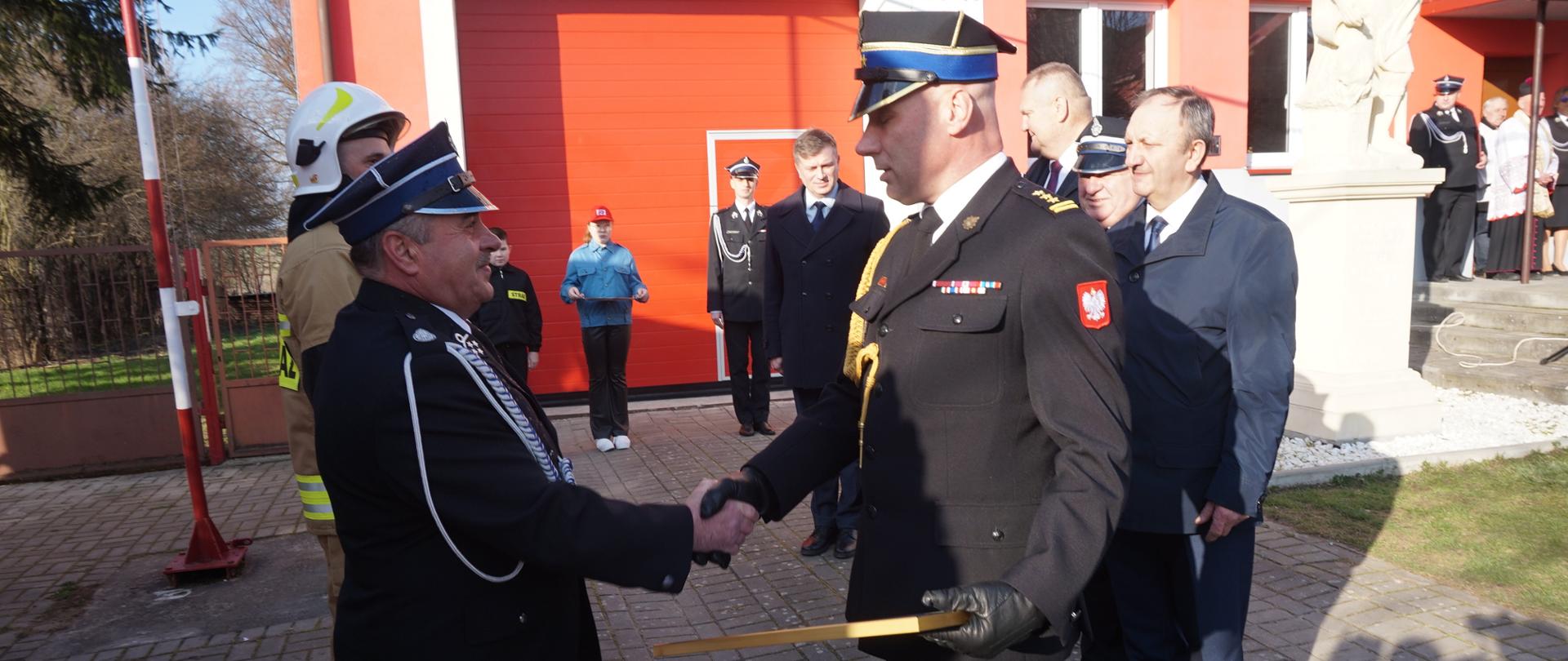 Przekazanie aktu wręczenia samochodu Prezesowi OSP Lasocin przez zastępcę komendanta wojewódzkiego PSP w Kielcach. W tle delegacja zaproszonych gości, druhowie OSP oraz przybyli goście 