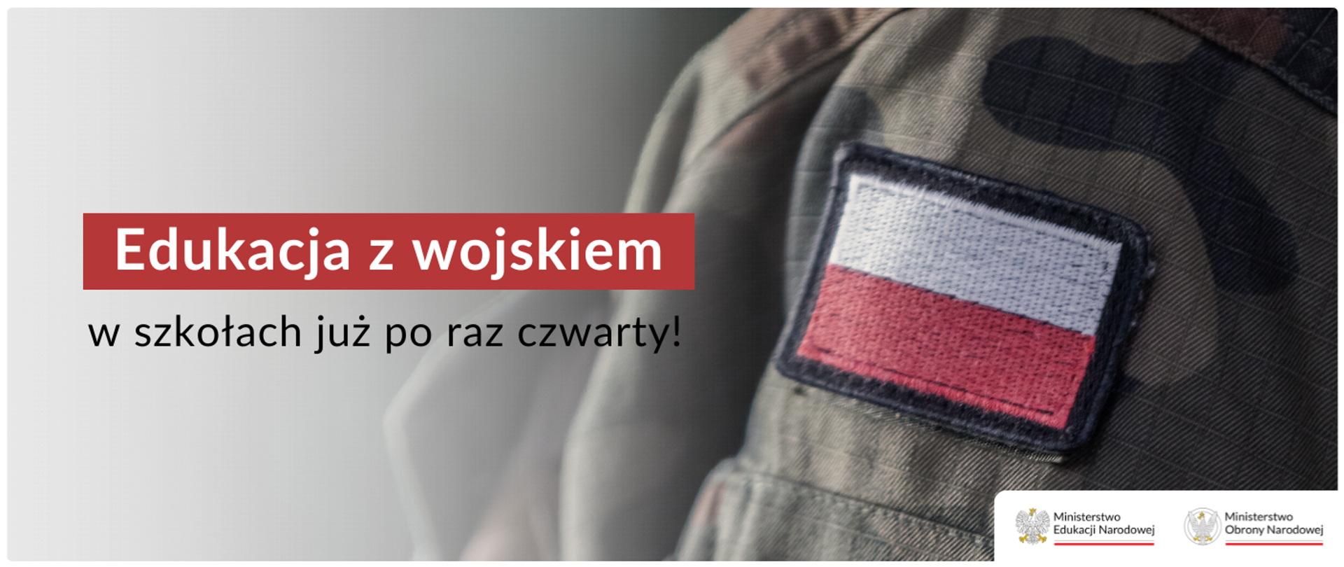Zbliżenie na ramię żołnierza w mundurze w barwach maskujących, z naszywką z polską flagą na rękawie. Na lewej stronie zdjęcia, na jasnym tle, widnieje napis w kolorze czerwonym i czarnym: 'Edukacja z wojskiem' oraz 'w szkołach już po raz czwarty!'. W prawym dolnym rogu znajdują się loga Ministerstwa Edukacji Narodowej i Ministerstwa Obrony Narodowej.