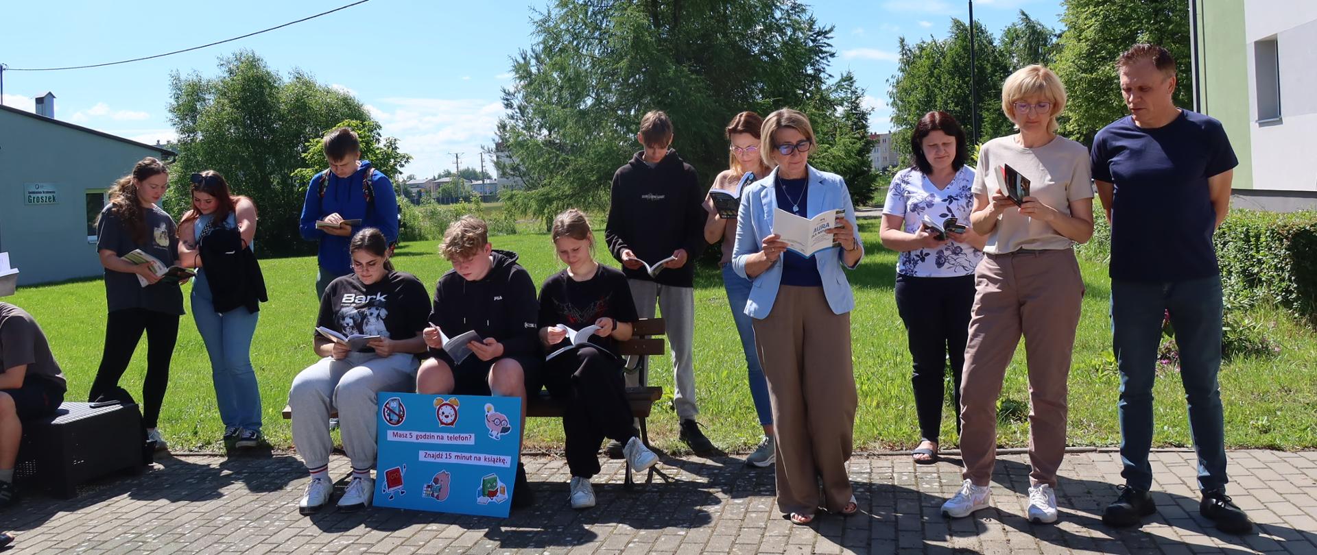 Uczniowie i nauczyciele czytający książki na świeżym powietrzu.