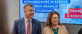 Minister Wieczorek i kobieta w szarożółtej bluzce stoją pod wielkim ekranem z napisem Różnorodność w szkole.