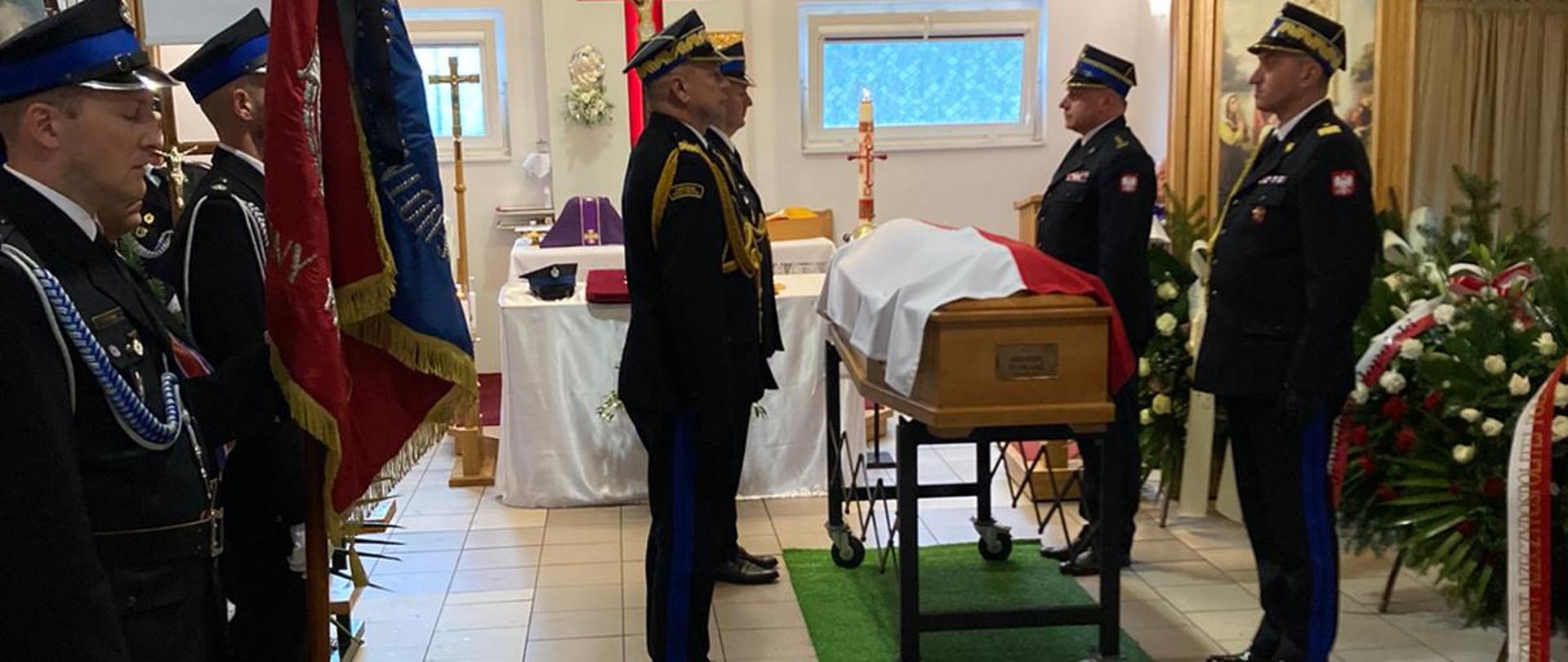 Na zdjęciu widać strażaków pełniących posterunek honorowy przy trumnie zmarłego strażaka. 