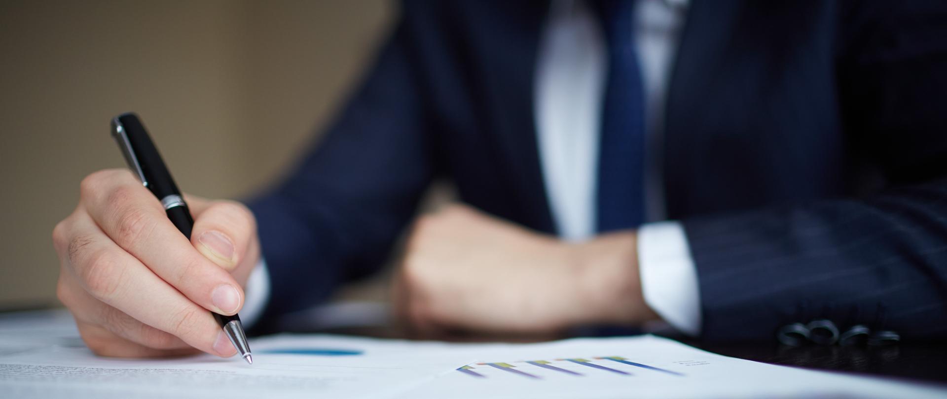 Image of human hand with pen over documents at workplace