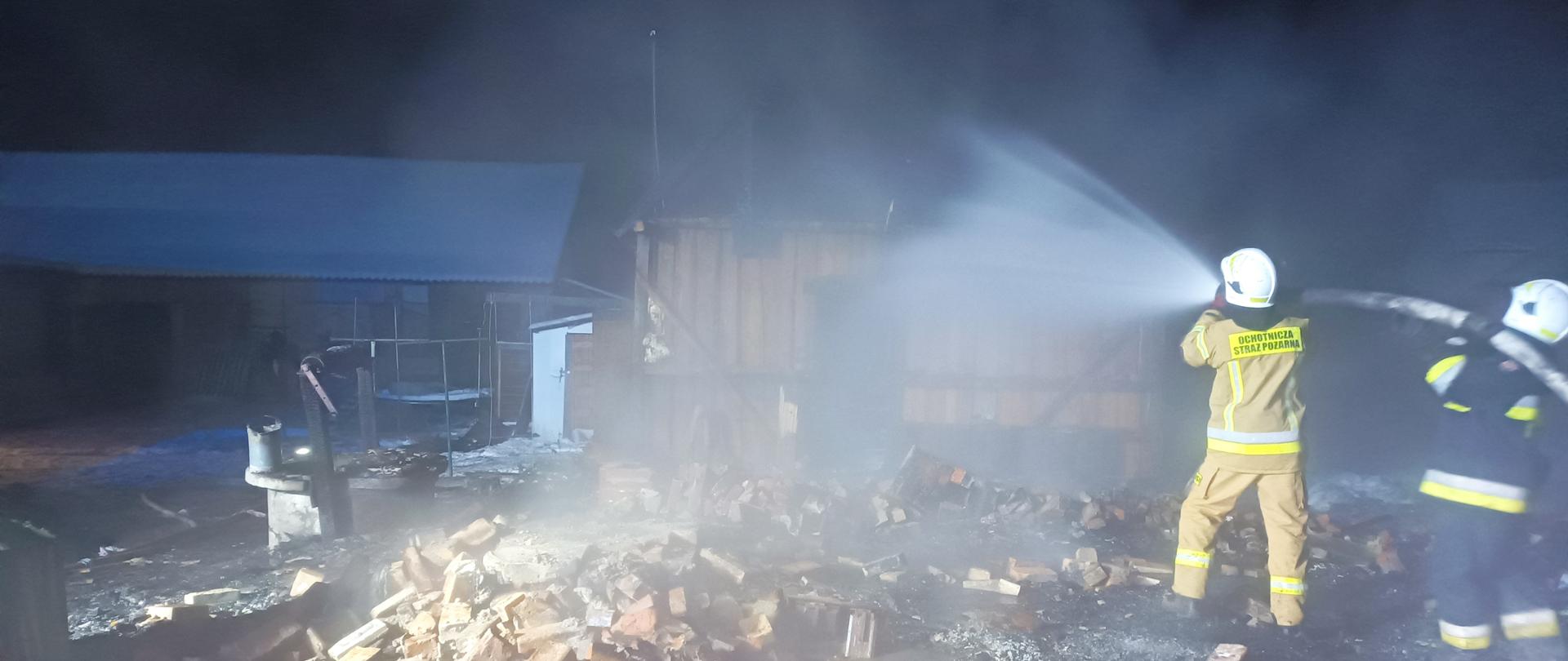 Pogorzelisko po pożarze. Strażacy dogaszają nadpalone elementy konstrukcyjne czesci gospodarczej budynku mieszkalnego. 