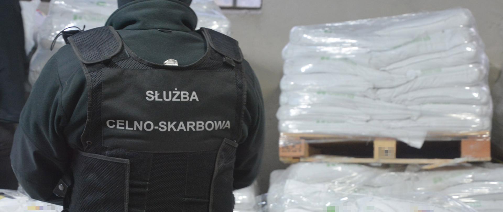 Funkcjonariusz Służby Celno-Skarbowej stojący tyłem, w tle zabezpieczone narkotyki