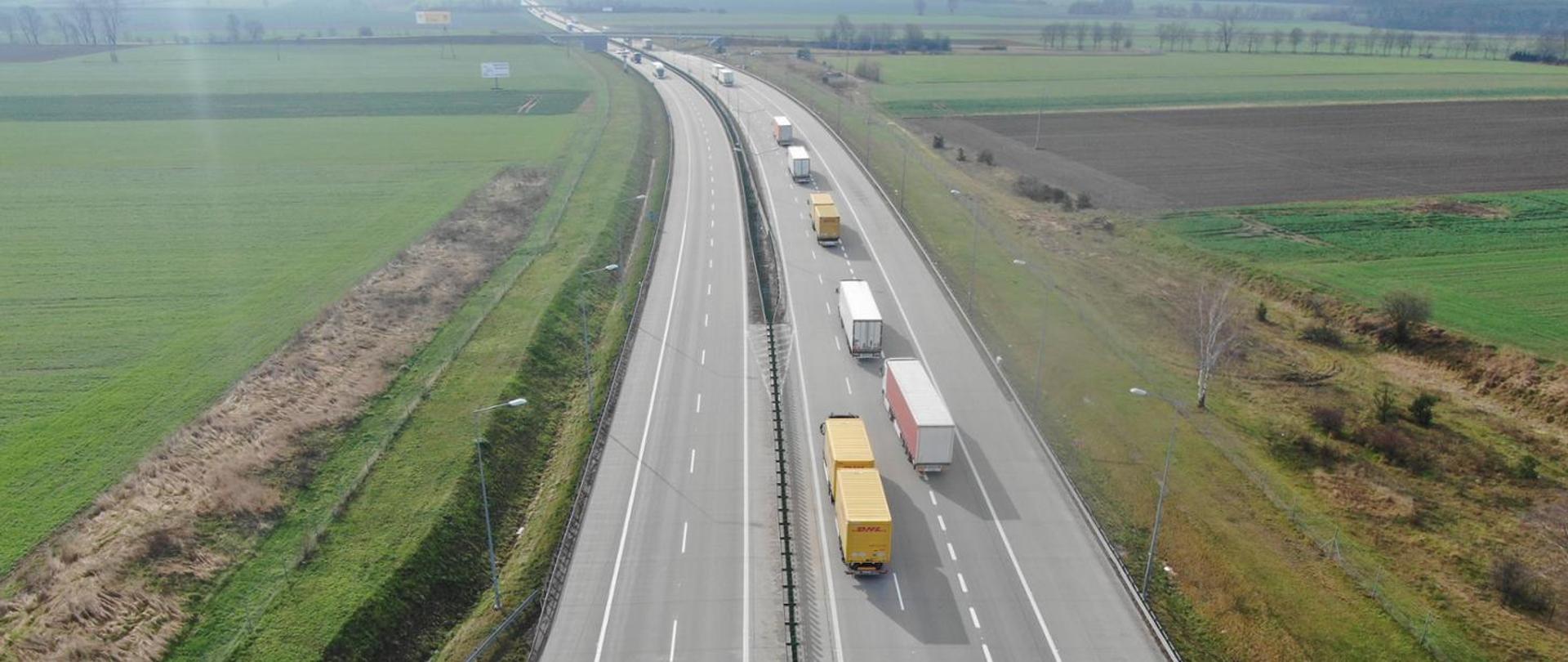 na zdjęciu widoczne dwie jezdnie autostrady, po której poruszają się pojazdy. Po obu stronach drogi łąki i pola
