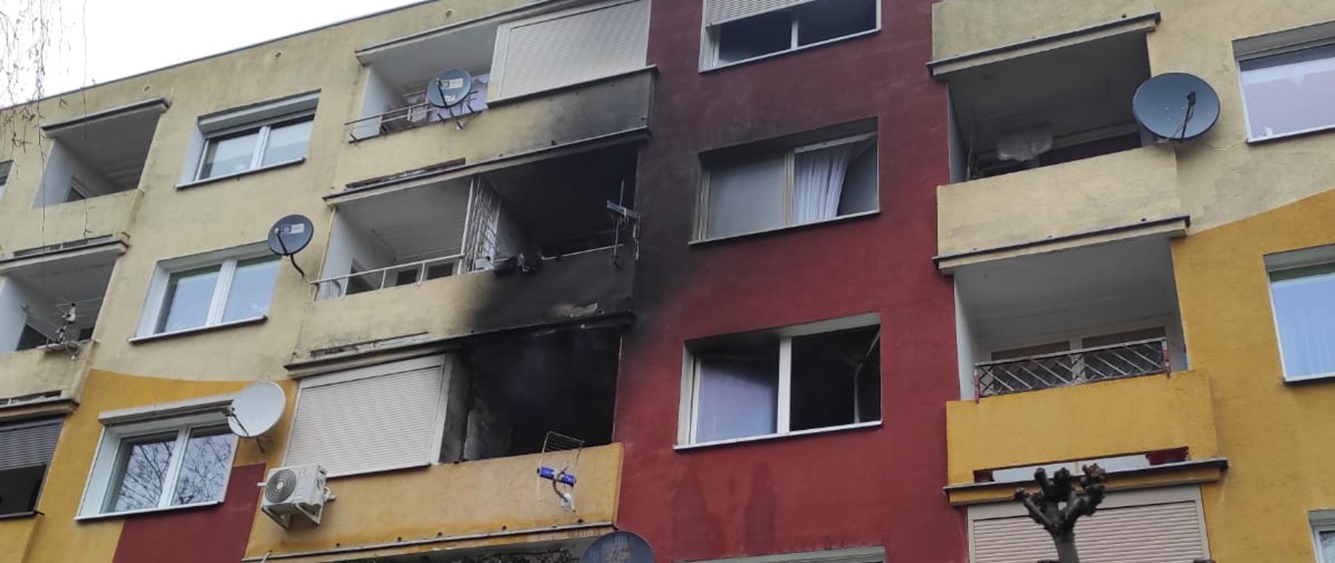 Na zdjęciu widzimy blok mieszkalny z kolorową elewacją. Jedno z mieszkań okopcone po pożarze.