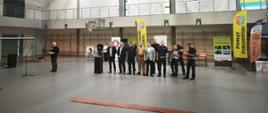 Zdjęcie przedstawia inaugurację akcji profilaktyczno-edukacyjnej „Bezpieczna droga do szkoły”, zorganizowanej w hali sportowej dla dzieci i młodzieży. W wydarzeniu uczestniczą funkcjonariusze policji oraz przedstawiciele lokalnych władz Powiatu Żuromińskiego, którzy przypominają najmłodszym o zasadach bezpiecznego poruszania się po drogach