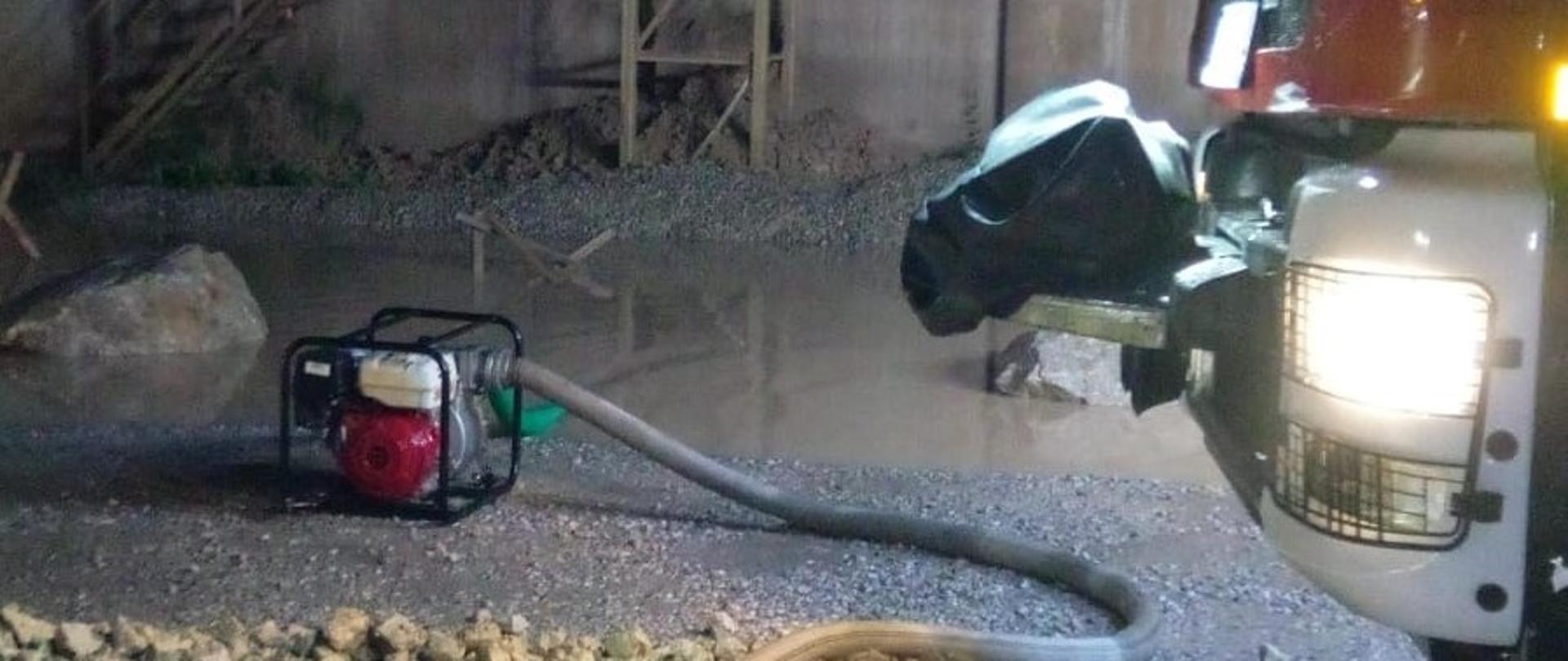 Zdjęcie przedstawia teren kopalni Miedzianka w Gałęzicach. Po prawej stronie widać fragment samochodu pożarniczego. W centralnym punkcie widać pompę, która wypompowuje wodę poza teren kopalni.