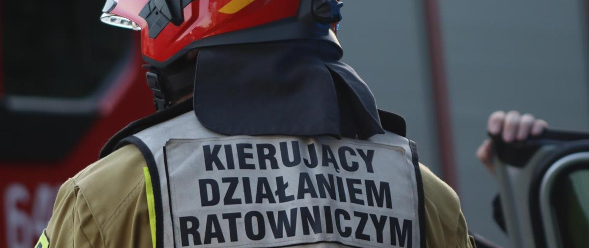 Na zdjęciu strażak w ubraniu specjalnym, ubrany w kamizelkę z napisem "Kierujący działaniem ratowniczym"