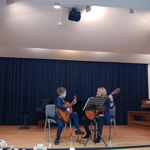 Zdjęcie przedstawia chłopca i kobietę , trzymają gitary , na granatowym tle.