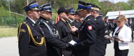 Na zdjęciu widoczni Małopolski Komendant Wojewódzki PSP i komendant powiatowy PSP w Gorlicach wręczający strażakom odznaczenia resortowe. Komendanci w galowych granatowych mundurach i w czapkach rogatywkach. Strażacy odbierający odznaczenia ubrani w galowe granatowe mundury i w czapkach rogatywkach oraz jeden w ubraniu koszarowym koloru czarnego w czapce.