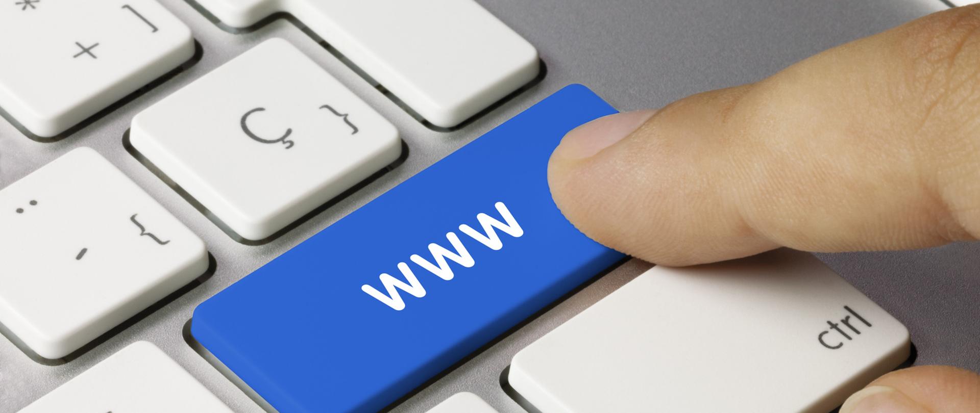 Fragment klawiatury komputera, palec nad niebieskim klawiszem z literami www
