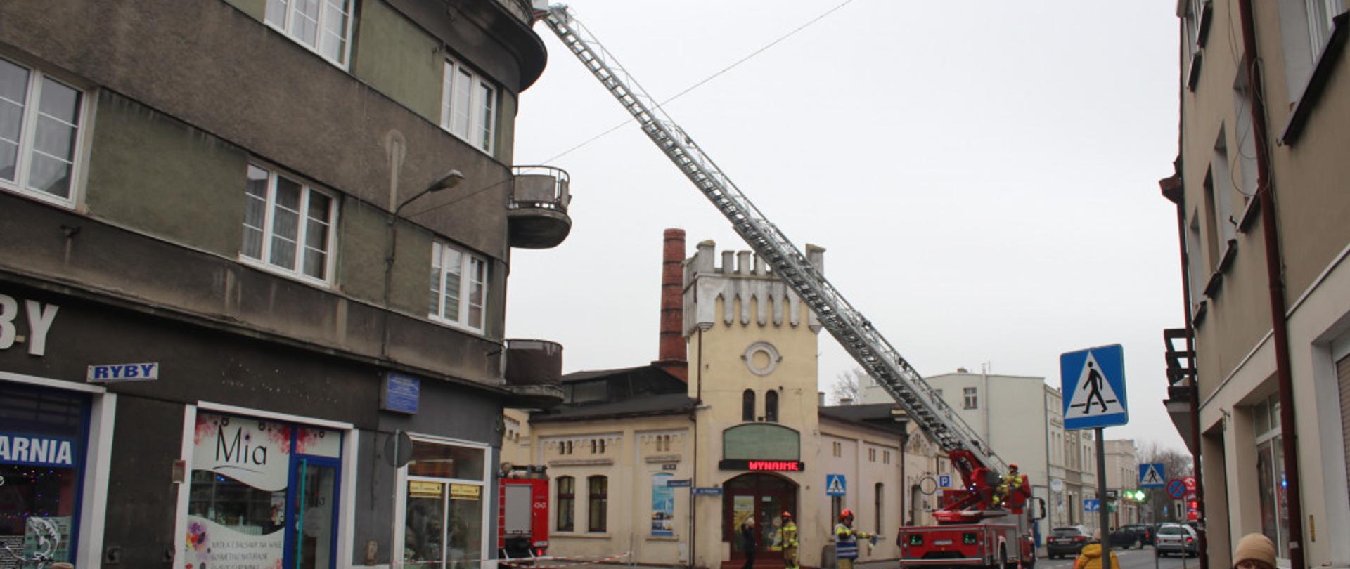 Zdjęcia przedstawia drabinę mechaniczną SD-31, która stoi na drodze. Strażacy usuwali szkody po silnym wietrze, który uszkodził dach budynku.