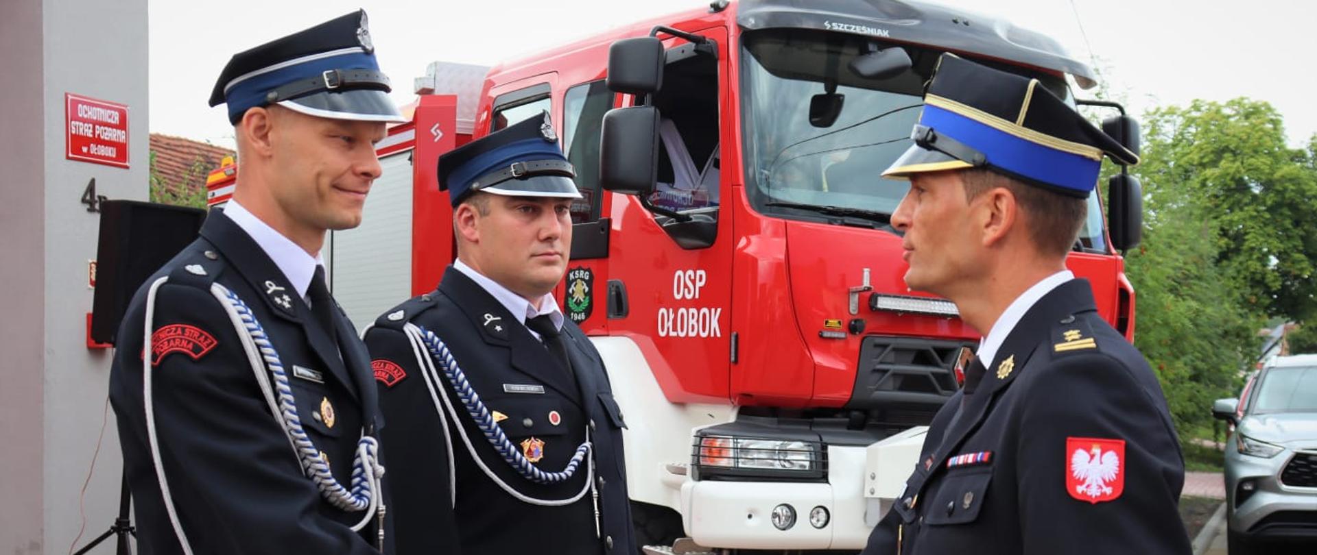 Przekazanie nowego samochodu ratowniczo-gaśniczego dla OSP Ołobok - na pierwszym planie zastępca LKW wręcza akt przekazania, samochód gasniczy w tle