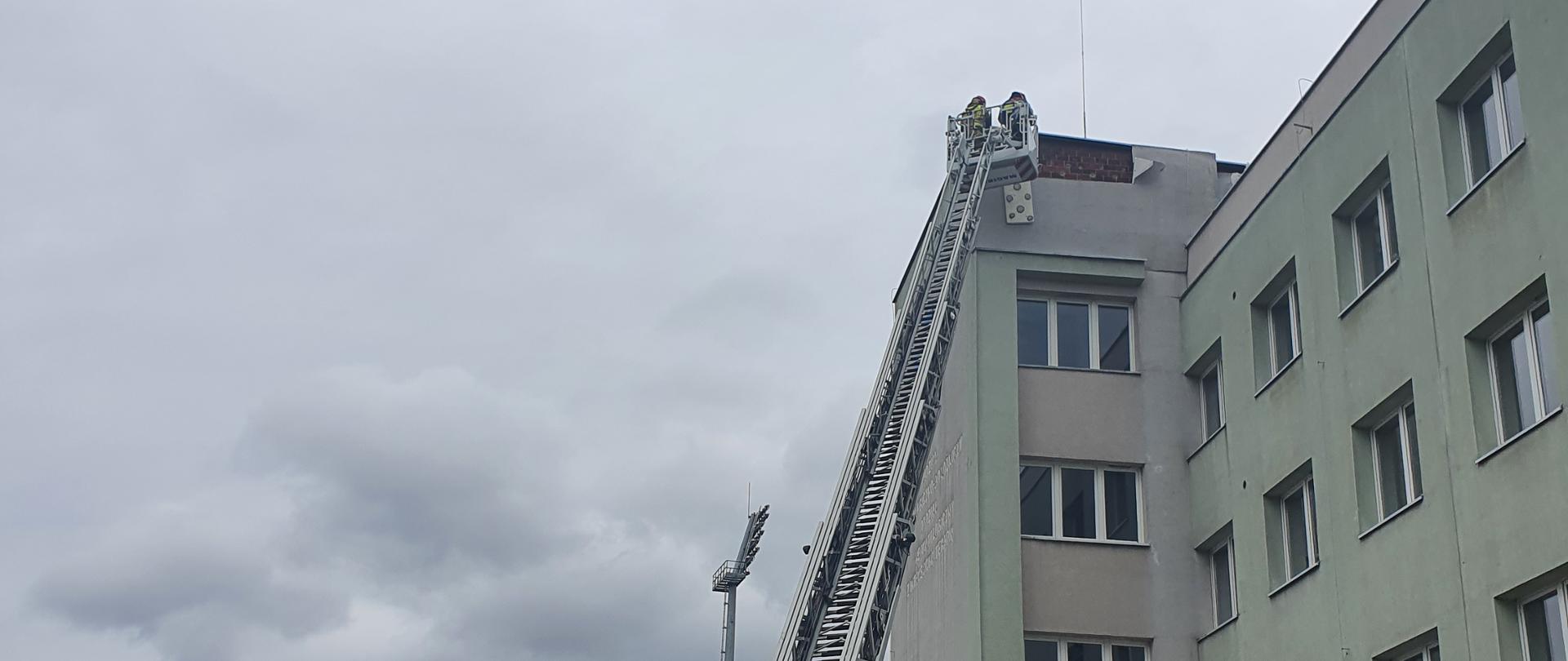 Drabina mechaniczna rozstawiona przy budynku szpitala. W koszu drabiny dwóch strażaków.