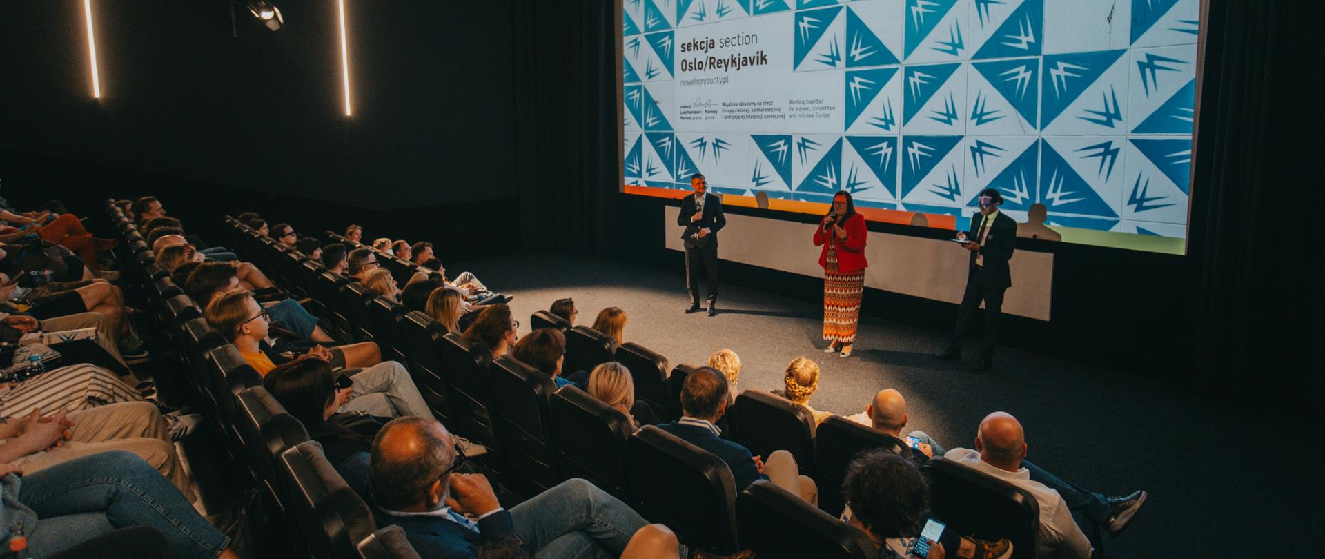 W sali kinowej publiczność. Na scenie trzy osoby. Wśród nich wiceminister Małgorzata Jarosińska-Jedynak.