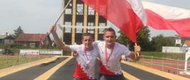 Zdjęcie obrazuje strażaków ze Skarżyska-Kamiennej trzymających flagi Polski. Stoją oni na torze do wspinania przy użyciu drabiny hakowej. Na ich szyjach wiszą medale. Wokół widać infrastrukturę stadionową.